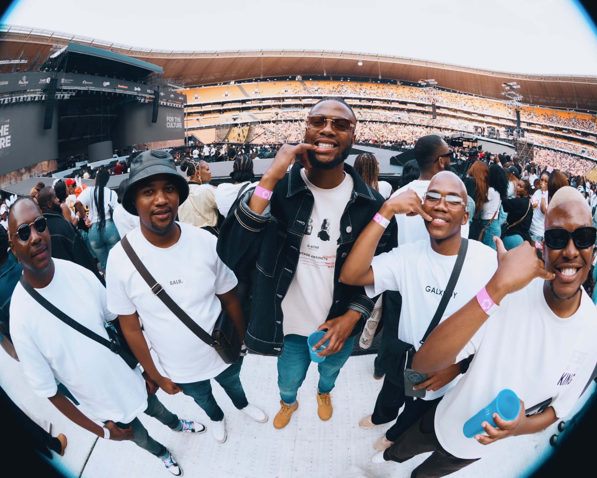 Group of friends in white tees on the field in front of the stage