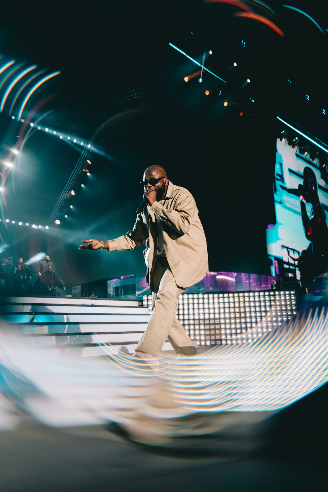Performer in beige striding across the stage through light streaks