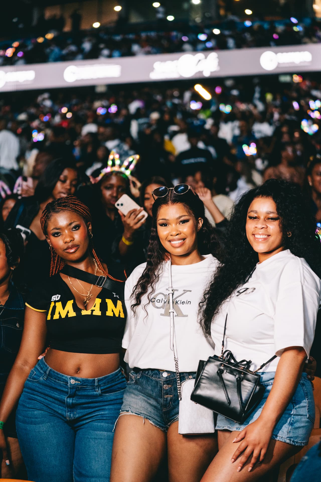 Three friends posing in the carnival crowd under the stadium lights