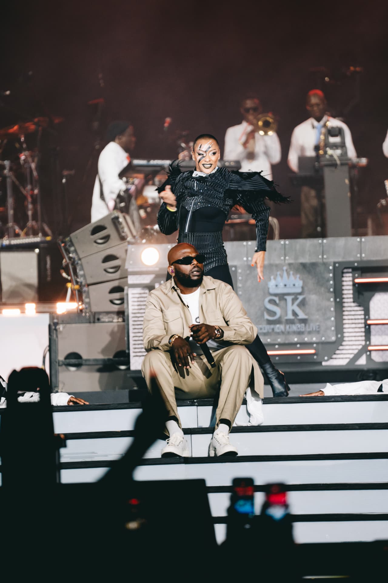 Scorpion King seated on stage while a dancer performs behind