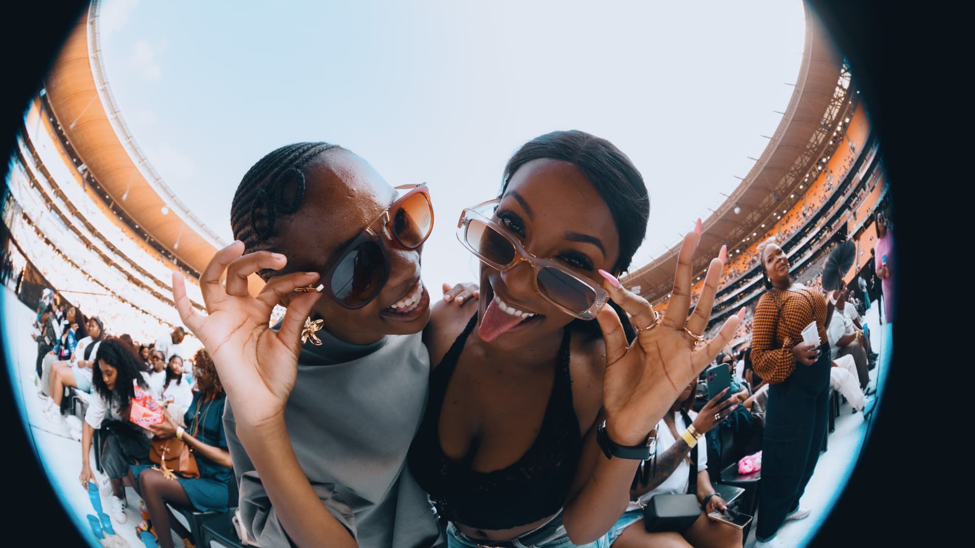 Two friends pulling faces in sunglasses in the stadium stands